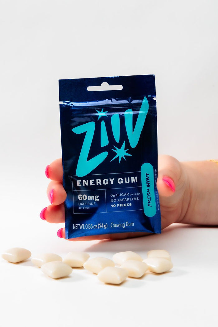 Una mano sosteniendo un paquete de chicle energético Ziiv Fresh Mint con piezas de chicle al frente